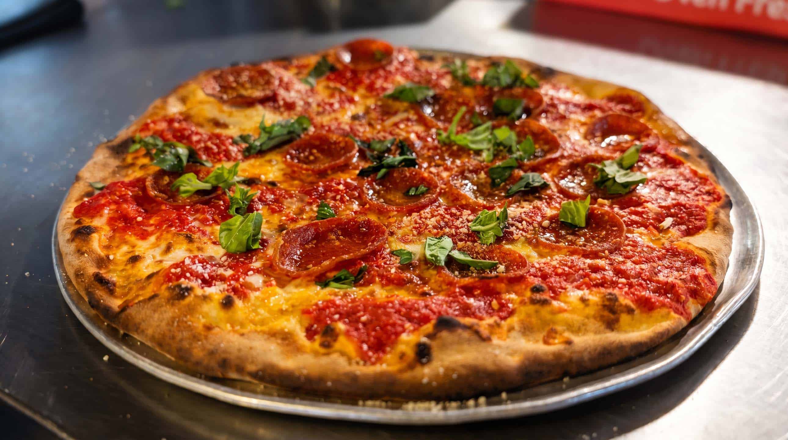 Fresh wood-fired pepperoni pizza with basil on a metal tray